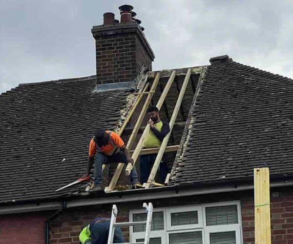 This is a photo of a roof repair being carried out. A section of the roof has been stripped and two roofers are replacing the rafters. Works being carried out by LPO Roofing Kempston